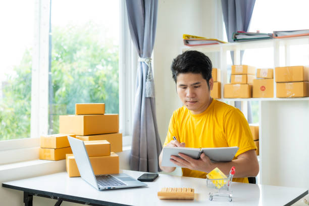 istock small business owner Asian man using mobile app on smartphone is checking parcel boxes, doing retail, parcel delivery, SME, online shopping. 2070917223