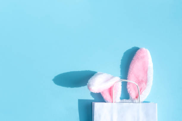白い紙袋から突き出たパステルカラーの背景にふわふわのウサギの耳。イースターショッピングのコンセプト。上面図、テキスト用のスペース。 - rabbit ear antenna ストックフォトと画像