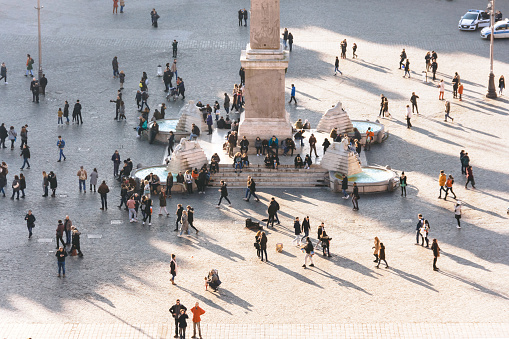 Busy Piazza della Repubblica with people walking, sun casting shadows, a central monument and fountain, urban hustle against historical backdrop. December 30, 2018. Rome, Italy