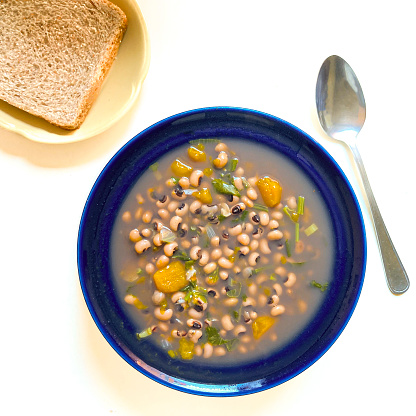 High angle view of delicious beans soup with vegetables for lunch made at home , ready to eat. Spoon and wholegrain bread in a small yellow plate.