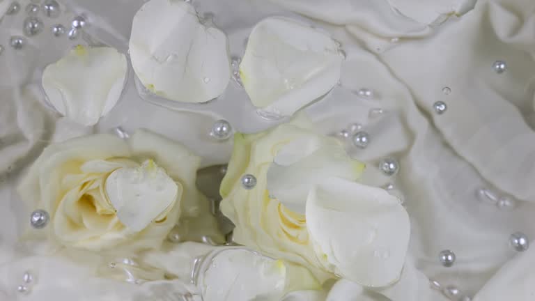 Pearls and white rose petals float on the surface of the water against the background of rose flowers underwater.