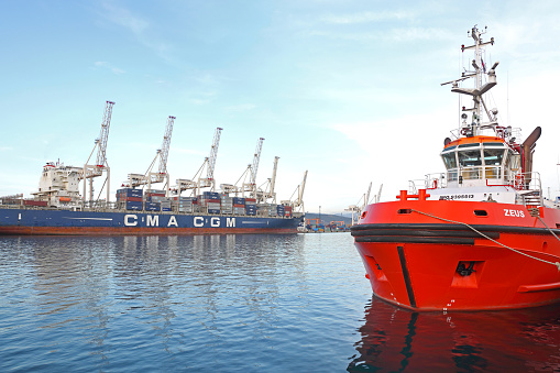 Koper, Slovenia - October 14, 2014: Red Tugboat and Long Container Ship Cma Cgm at Cargo Port.