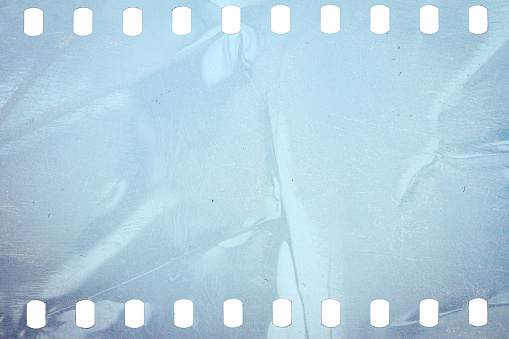 Dusty and grungy 35mm film texture or surface. Perforated scratched camera film isolated on white background.