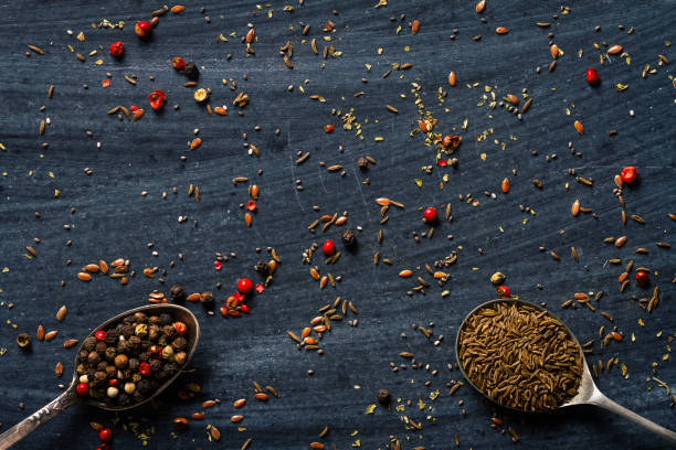 A top-down view of aromatic spices and dried tea leaves arranged on a white background. The composition features star anise, black peppercorns, and two small ceramic bowls filled with dried tea leaves, creating a minimalist yet elegant food presentation. The scattered elements add an organic feel, emphasizing the rich textures and natural beauty of these culinary ingredients. This image is ideal for use in food blogs, tea packaging designs, spice advertisements, or educational content about traditional herbs and spices.
