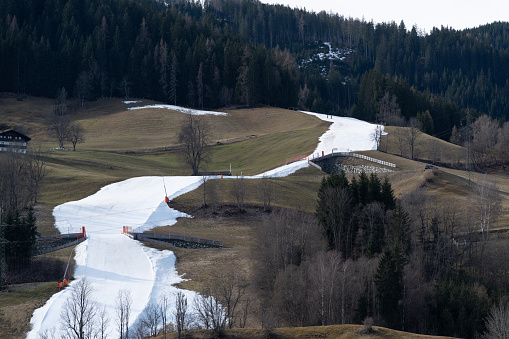 negative visible impacts of global warming for winter sport tourism skiing, fake snow ski slope in between mountain meadow during first days in march 2024 in austria, europe