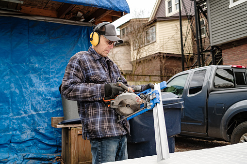Senior man doing carpentry hobby project in his outdoor wood shop. Back yard of city residence in Toronto, Canada during winter with no snow.