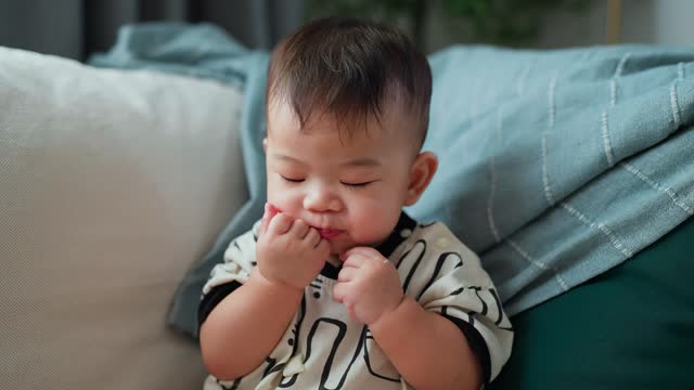 Cute little boy sit sofa in living room and eating rice snack bar.  Asian toddler boy enjoying eating snack at home in living room early in the morning A baby boy eats a rice cracker