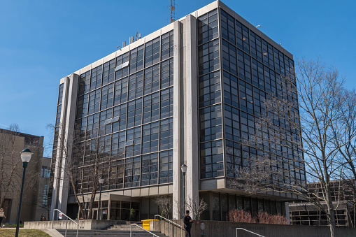 Low angle view on building exterior with uneven windows in rows, diminishing perspective towards the sunny sky, abstract background