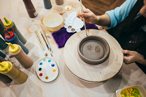 Close-up of a woman's hands painting pottery, the footprints of her little feet are those of her puppy