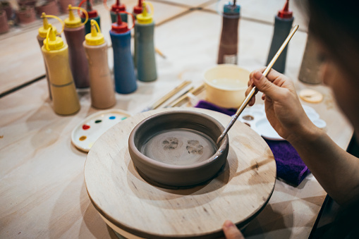 Close-up of a woman's hands painting pottery, the footprints of her little feet are those of her puppy