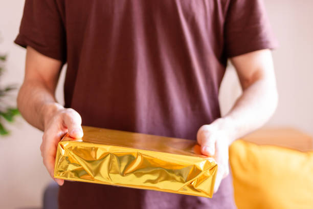 Close-up of hands presenting a wrapped golden gift box