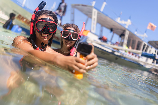 Two smiling female friends with diving goggles filming themselves with a wearable camera