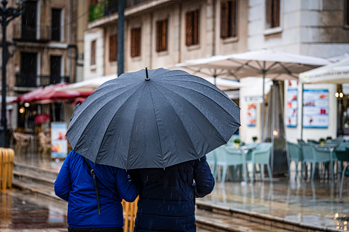 a beautiful young couple of tourists, walking in the rain with a suitcase and a large umbrella