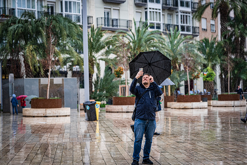 Valencia, Spain. March 9, 2024. Torist taking pictures under the rain using umbrella