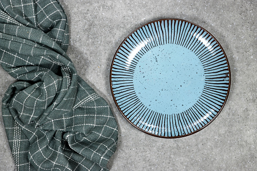A blue plate with a checkered cloth underneath it. The plate is placed on a grey grunge background