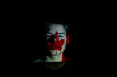 Portrait of a young man with a Canadian flag projected on his face against a black background