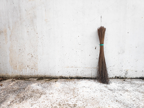 The art Photographic image of an old broom stick propped against an old white wall.