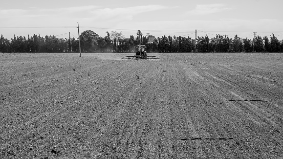 Black and white image of a tractor plowing in the middle of the field.