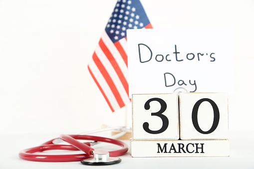 Text Doctor's Day with cube calendar and stethoscope on white background