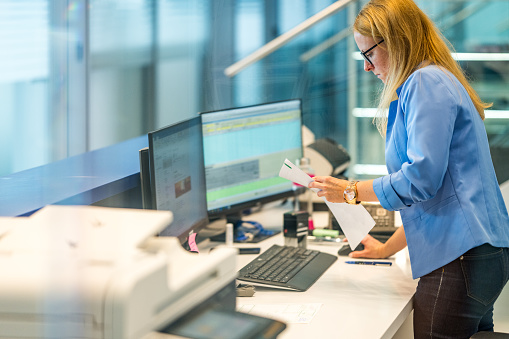 Side view photo of a white female receptionist working at her desk in a modern office hallway.