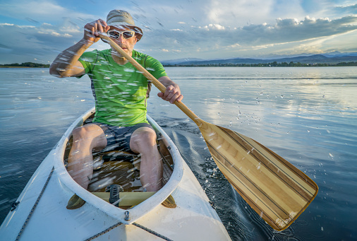 senior male paddler paddling  a decked expedition canoe with a water splash on a lake in northern Colorado