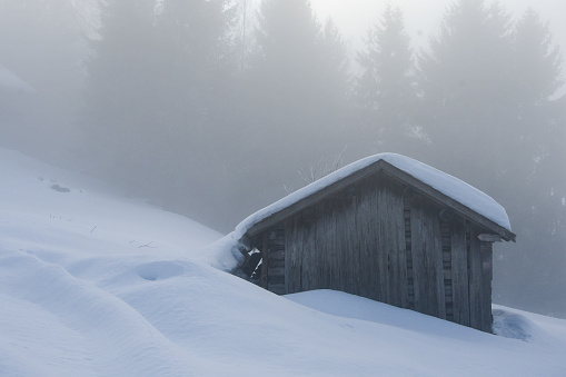 A small mountain cottage or house during fog and snow in winter
