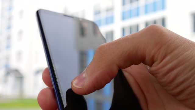 Close-up of a smartphone in the hand of a man typing a message outdoors