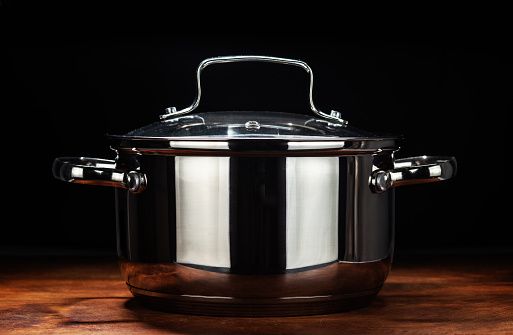 A new stainless steel pan is on an wooden table against a black background.
