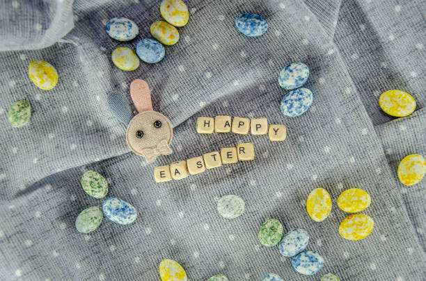 Easter concept. Easter egg shaped candies, cotton rabbit, Happy Easter letters on a cotton dotted tablecloth.