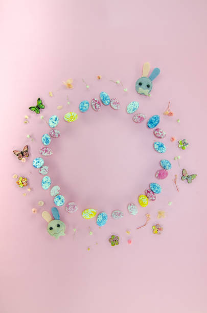 Easter celebration composition. Top view of a frame made of easter egg candies, small flowers isolated on pastel pink background. Easter concept. Flat lay, top view, copy space