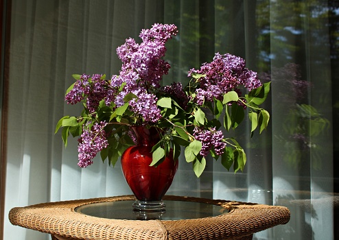 Bouquet of lilacs in a glass vase standing on a small wicker table.