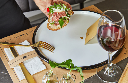 A stylish hostess in a modern kitchen elegantly places a delicious dish of carpaccio on bread on a clean marble countertop, demonstrating the art of presentation and culinary prowess.