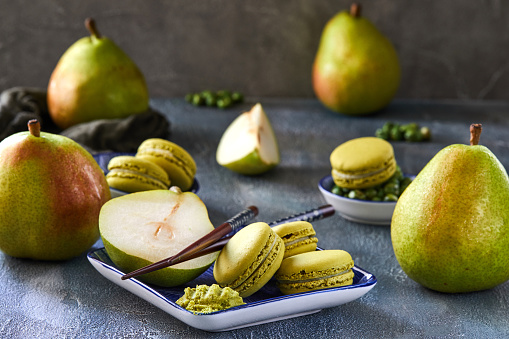 Green matcha macarons with sliced ripe pears on a blue plate, set on a stone table. Represents a healthy lifestyle with organic desserts. Close-up view showcases the delicious presentation.