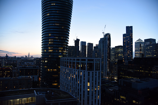 London Cityscape with the Canary Wharf business district. The image shows several tall business buildings with cloudy sky, captured during summer season at dusk.