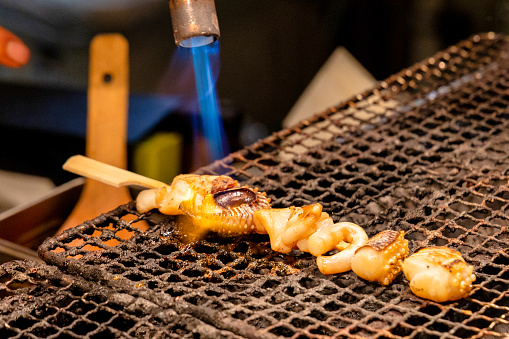 A close up of Octopus and Squid Skewers being blow torched.