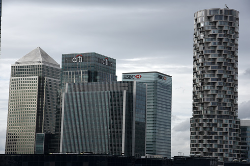 London Cityscape with the Canary Wharf business district. The image shows several tall business buildings with cloudy sky, captured during summer season.