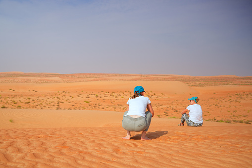 Two senior women one siting and other squat down on Wahiba desert sand in Oman. They are looking to the horizon, only sand and sky.