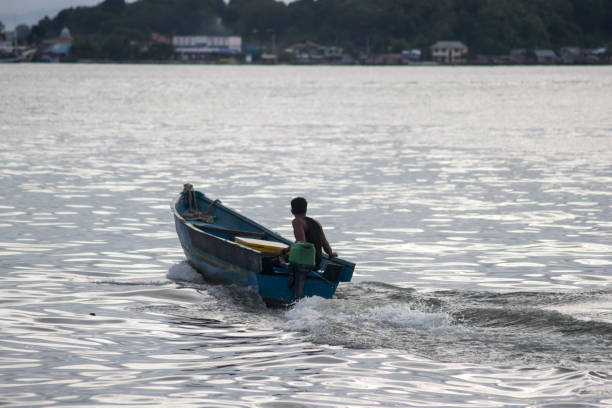 Sorong, Southwest Papua, Indonesia, 06/16/2021. The atmosphere of a crowd of people at a traditional fish market on the edge of the fishing pier. A fisherman driving a motorboat is approaching the dock
