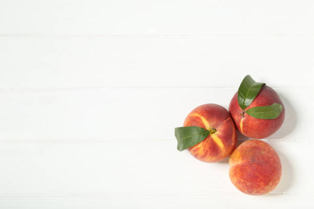 istock Fresh peaches with green leafs on white wooden table 2071507669
