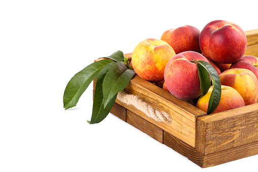 Fresh peaches with green leafs in crate isolated on white background