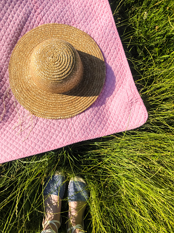 Summer flat lay. Picnic blanket, hat, woman legs on green grass. Top view from above. Summer holiday vacation resting concept. Happy sunshine day. straw hat lies on pink blanket. Girl shoes sandals
