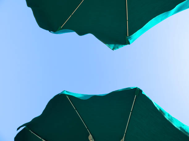 Green beach umbrella. Blue sky in the background. View from below. Relaxing context. Summer holidays by the sea. General contest and location