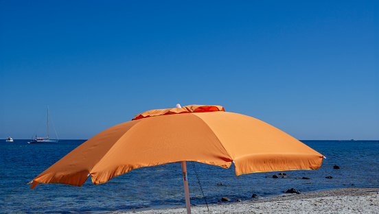 Orange beach umbrella. Blue sky. Relaxing context. Summer holidays at the sea. General contest and location