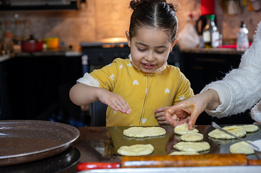 Cheerful kid helping mother in preparing pastries in kitchen , preparing food together