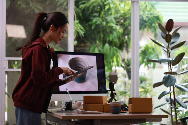 Craftswoman with tablet standing in pottery workshop photographs handmade clay products studio.