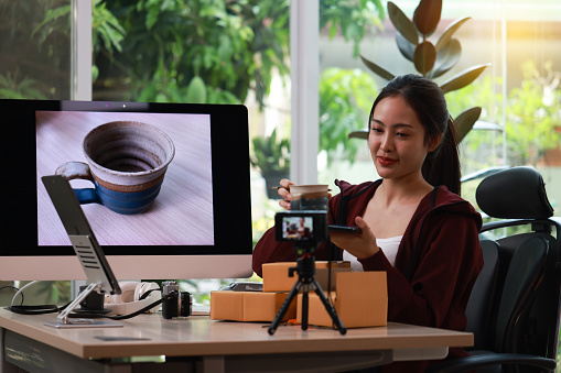 A confident Asian craftswoman bidding on Handmade porcelain cups online live streaming in the pottery studio