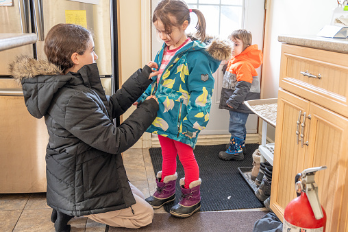 Teenage girl helping little girl to dress-up before getting outside to play during winter day