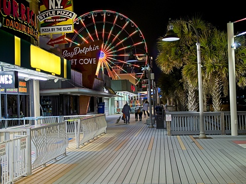 Myrtle Beach, South Carolina - USA, February 21, 2024. Myrtle Beach at night during the cooler offseason. Business lined with Ferris wheel in distance.