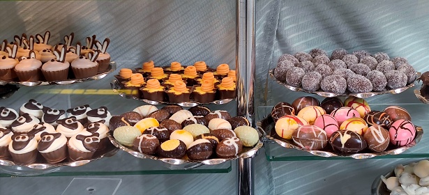 Different types of Easter chocolate, such as Easter eggs and other luxury Easter chocolates are in a display case in a shop window in a chocolate shop. There are no persons or trademarks in the shot.