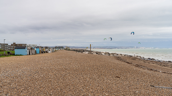 Lancing, West Sussex, England, UK - October 04, 2022: Beach huts on the beach and kite surfers